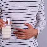 Man with stomach pain holding a glass of milk. Dairy Intolerant person. Lactose intolerance, health care concept.